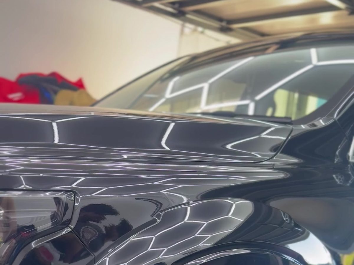 Black ute bonnet and guard with garage lights reflected in deep gloss paint