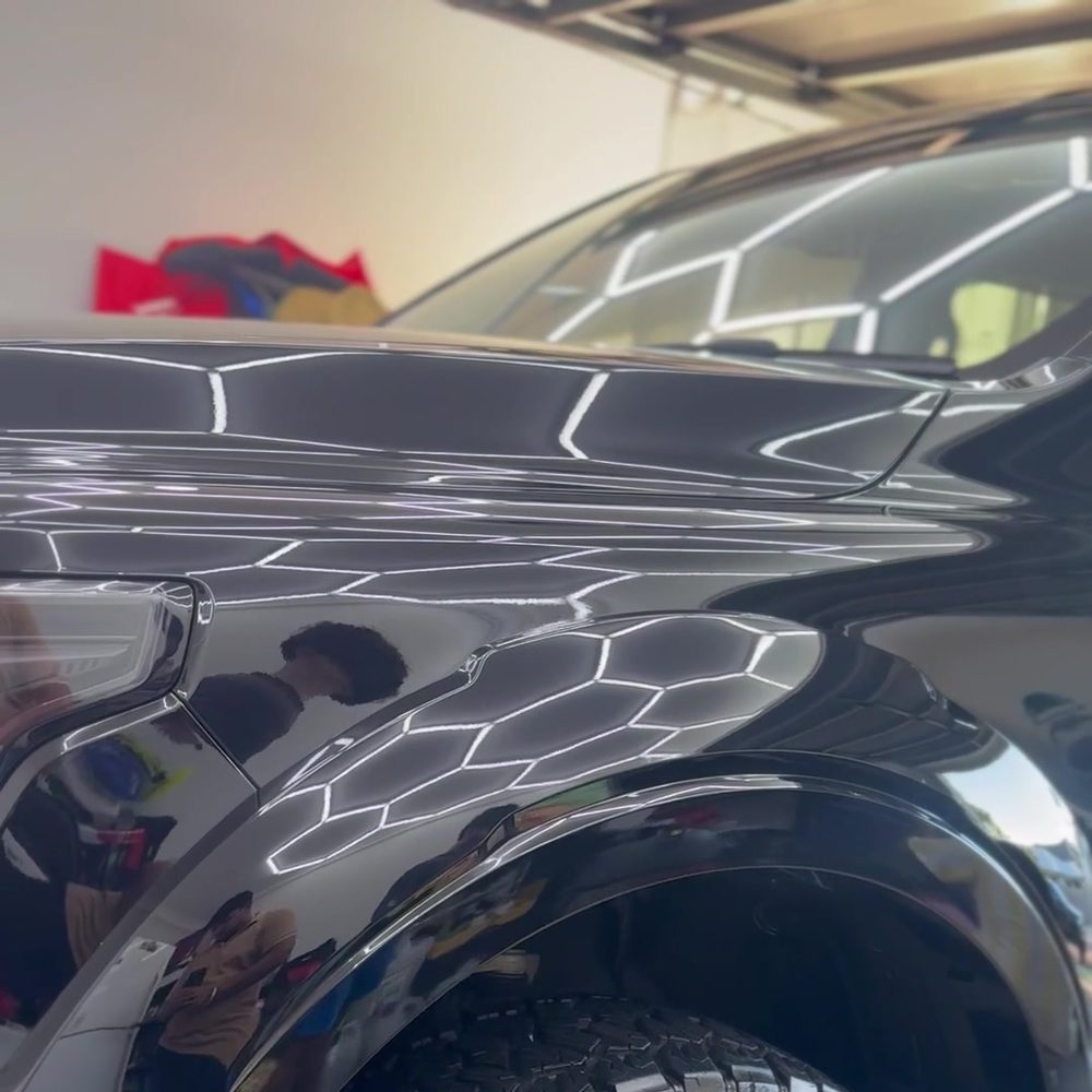Black ute bonnet and guard with garage lights reflected in deep gloss paint
