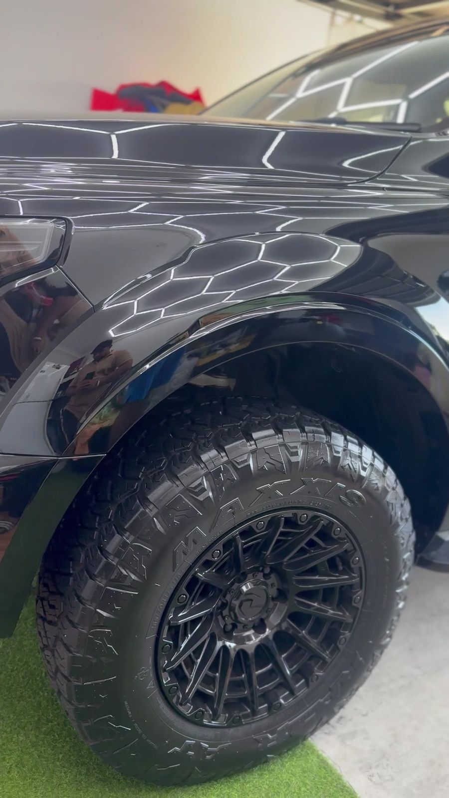 Black ute guard and tyre with garage lights reflected in the paint